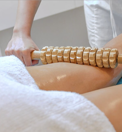 Une femme utilise le rouleau en bois de madérothérapie sur la jambe de la cliente